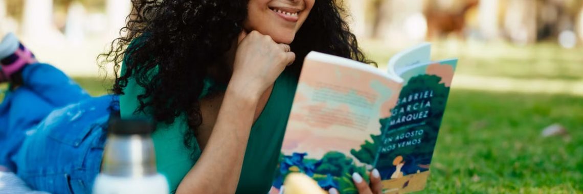 Smiling woman reading a book at a picnic in a sunny park setting.