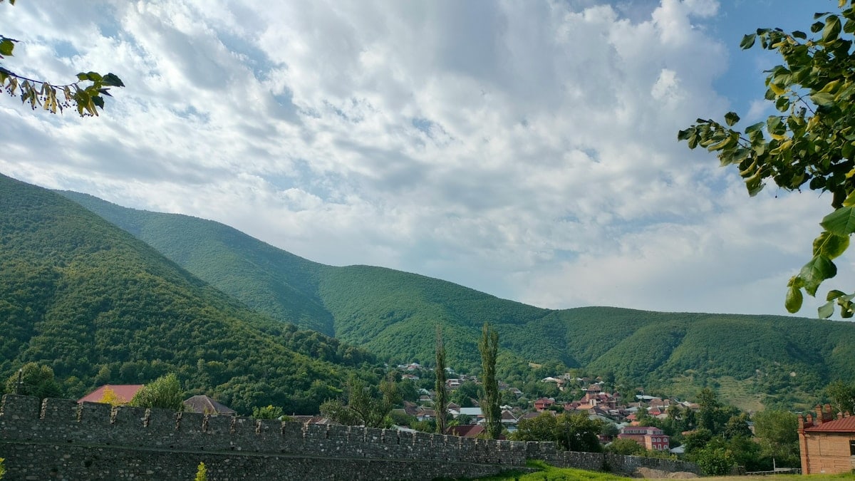 Lush green mountains with a village and stone wall.